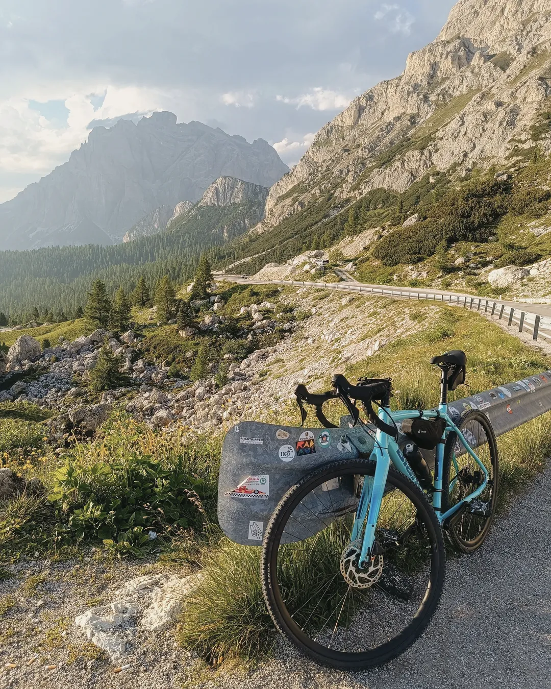 Una bicicletta appoggiata al guardrail di una strada di passo, tra prati e pareti di roccia nella luce della sera